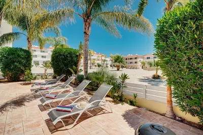 a row of chaise lounge chairs and palm trees at Apartment Helena in Ayia Napa