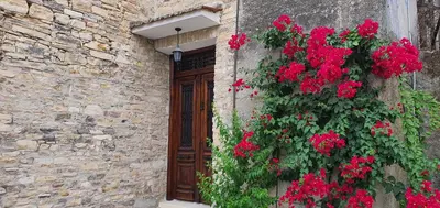 a stone building with red flowers and a wooden door at Bougainvillea House Lefkara in Pano Lefkara