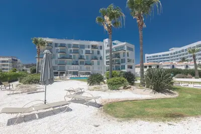 a hotel with chairs and an umbrella and palm trees at Protaras Thalassa Apartment Ta206 in Protaras