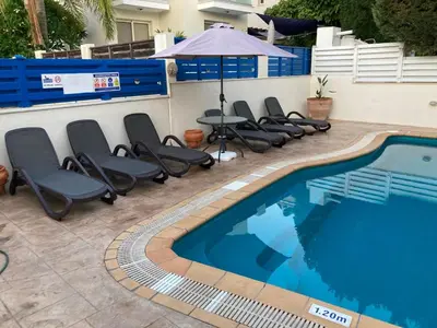 a pool with chairs and an umbrella next to a building at Anna Villa in Protaras