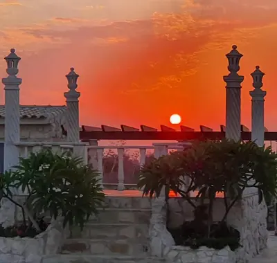 a sunset view of a building with palm trees at Oikos Selinolithos in Alaminos