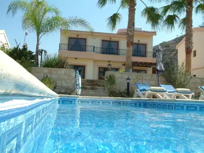 a swimming pool in front of a house with palm trees at Three bedroom villa with private pool and landscaped garden close to the beach in Pissouri