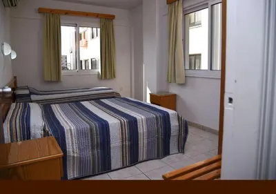 a bedroom with a striped bed and two windows at Elysso Apartments in Larnaka