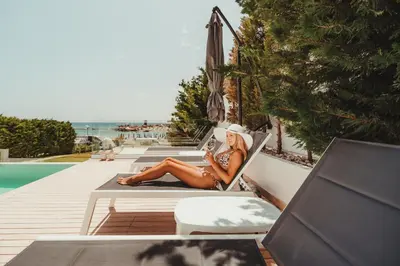 a woman sitting in a chair reading a book by a pool at Protaras Beachfront Villa Blue Waves in Protaras