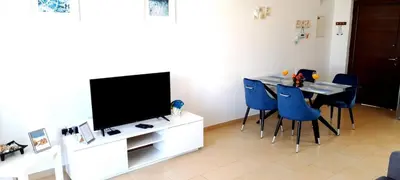 a living room with a tv and a table with blue chairs at Nissi 3 Pool View Apartment in Ayia Napa