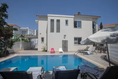 a swimming pool with chairs and a house at Pelagos Villa 8 in Protaras