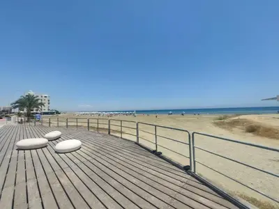 a wooden boardwalk on a beach with two white benches at Beach Serenity Studio on Makenzy in Larnaka