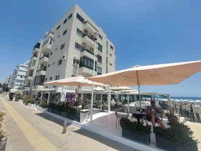 a woman sitting at a table under an umbrella next to a building at Beach Serenity Studio on Makenzy in Larnaka