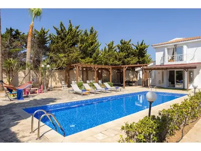 a swimming pool with lounge chairs and a house at Protaras Apollon Seaside Villa in Protaras