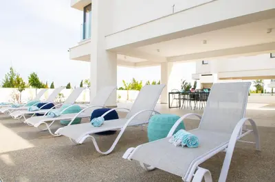 a row of white chaise lounge chairs on a patio at Billy's Place Protaras Luxury Villa with private pool with heated pool option for autumn and winter months in Paralimni