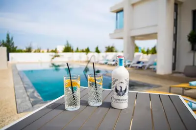 a bottle of wine and two glasses on a table by a pool at Billy's Place Protaras Luxury Villa with private pool with heated pool option for autumn and winter months in Paralimni