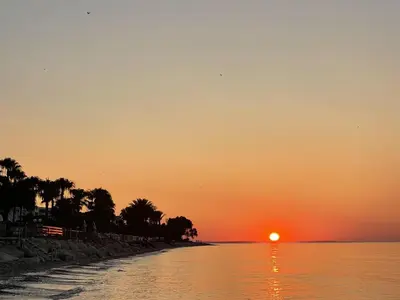 a sunset on a beach with the sun setting at Meneou Blu Beach House* in Meneou