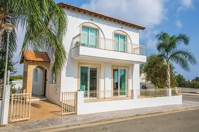 a white house with a balcony and palm trees at Villa Cayenne in Protaras