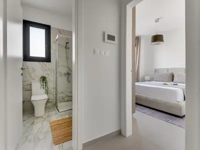 a white bedroom with a bed and a bathroom at Sanders Triple in Limassol