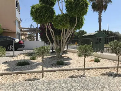a garden with trees and shrubs in front of a fence at Themis Beach Apartments in Larnaka