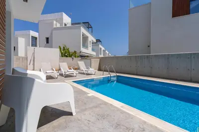 a swimming pool with white chairs next to a building at Villa Flora's 3-BR Retreat & Private Pool in Protaras in Paralimni