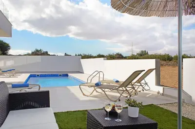 a patio with a pool and chairs and an umbrella at Villa Genesis in Protaras
