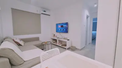 a white living room with a couch and a tv at STAY Napa Aura Apartment in Ayia Napa