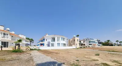 a row of houses on a beach with palm trees at Beach Vibes Beachfront Apartment in Pyla