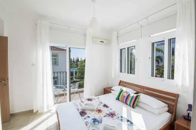 a white bedroom with a bed and a balcony at Villa Armostia in Protaras