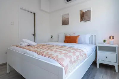 a white bedroom with a large bed with orange pillows at Hermes 2-Bedroom Apartment in Larnaca in Larnaka
