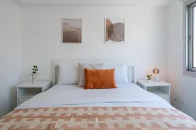 a white bed with an orange pillow on it at Hermes 2-Bedroom Apartment in Larnaca in Larnaka