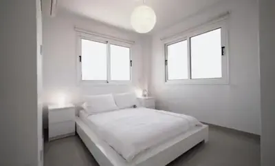 a white bedroom with a bed and two windows at Welcome to Thea Court in Paralimni