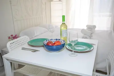 a white table with a bowl of fruit and a bottle of wine at Palmove Makenzie Studio 4 in Larnaka
