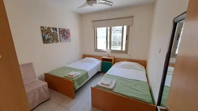 a room with two beds and a chair and a window at Dream Beach House Steps from the Sea & Free Parking in Protaras