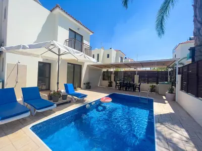 a swimming pool with blue chairs and a house at Fotini Villas in Protaras