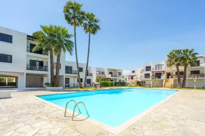 a swimming pool with palm trees in front of a building at Cozy Apartment In Kapparis in Paralimni