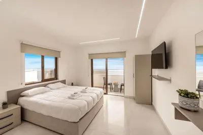 a white bedroom with a large bed and a television at SEVIS SUITES in Ayia Napa