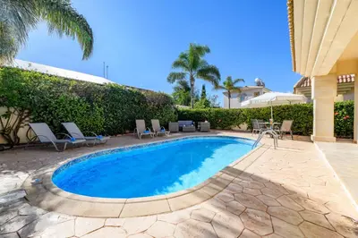 a swimming pool with chairs and a house at Villa Oscar in Protaras