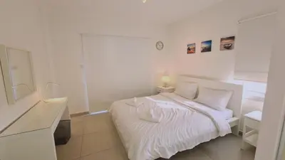 a white bedroom with a white bed and a mirror at STAY Beach Wave Apartment in Larnaka