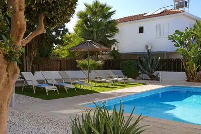 a pool with chairs and an umbrella next to a house at Villa Posidonia - 200m from Sandy Beach in Ayia Napa