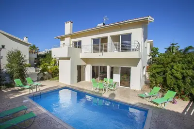 a villa with a swimming pool and green chairs at Theodora in Protaras
