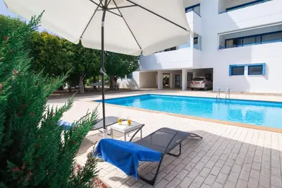 a pool with an umbrella and a chair and a table at The Good Times Apartment in Protaras