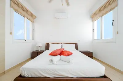 a white bed with two red pillows and two windows at Spacious Villa with Private Pool & Breathtaking Panoramic Ayia Napa views in Ayia Napa