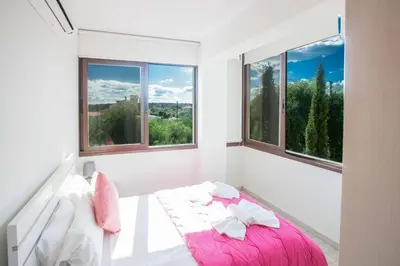 a white bedroom with windows and a pink bed at Protaras Demetra Villa DE1 in Protaras