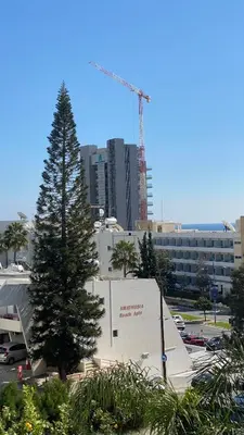 a pine tree in front of a building with a crane at T&L Apartments Agiaos Tychonas in Limassol