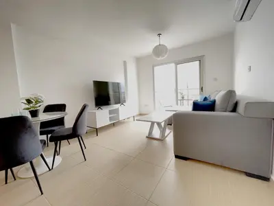 a white living room with a couch and a table at Sunset Pearl Holiday Apt. - Ayia Napa in Ayia Napa