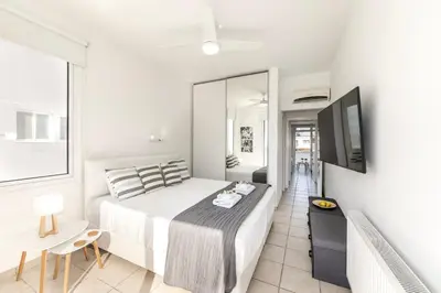 a white bedroom with a bed and a television at Faros Seaside Villa Larnaca in Pervolia