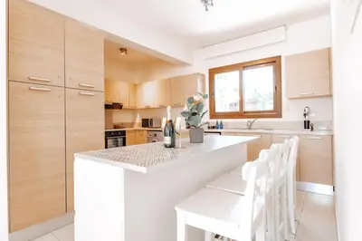 a kitchen with a white counter and white chairs at WealthyStays Sunset Villa, 3min walk to Sea in Paralimni
