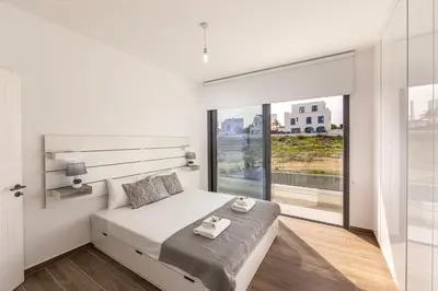 a white bedroom with a bed and a large window at Protaras By the Bay Villa 33 in Protaras