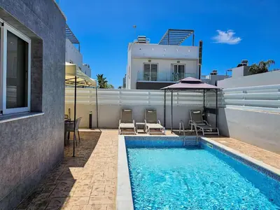 a swimming pool with chairs and an umbrella next to a house at Nissi beach villa Holiday in Ayia Napa