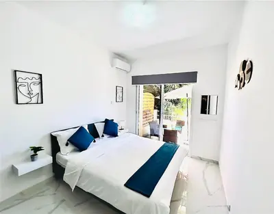 a white bedroom with a large bed with blue pillows at Nicolas 1 in Larnaka