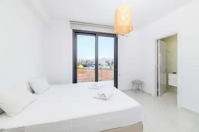 a white bedroom with a large white bed and a window at By The Beach - White Coral Villa in Protaras