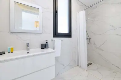 a white bathroom with a sink and a shower at By The Beach - White Coral Villa in Protaras