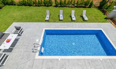 a swimming pool in a yard with two chairs and a table at By The Beach - White Coral Villa in Protaras