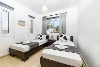 two beds in a room with two windows at Villa Clementine in Protaras